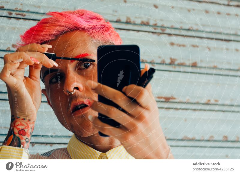 Stylish Homosexuell Make-up Wimpern gegen Smartphone auf grauem Hintergrund schwul Wimperntusche Mode ungewöhnlich feminin Porträt benutzend Mann Apparatur