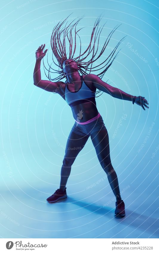 Schwarze Sportlerin mit fliegenden Haaren auf blauem Hintergrund fliegendes Haar Bewegung Kraft Afro-Look Geflecht muskulös Energie dynamisch Frau Vitalität