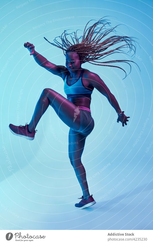 Schwarze Sportlerin mit fliegenden Haaren auf blauem Hintergrund fliegendes Haar Bewegung Kraft Afro-Look Geflecht muskulös Energie dynamisch Frau Vitalität