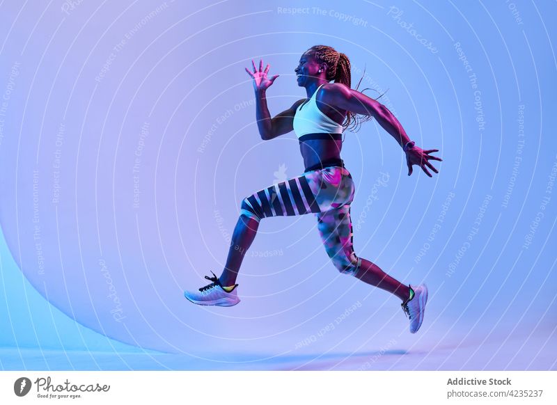 Aktive schwarze Sportlerin beim Laufen im Neonlicht laufen springen Aktivität schnell Training Bestimmen Sie Energie Frau dynamisch Läufer Herz Sprung Übung