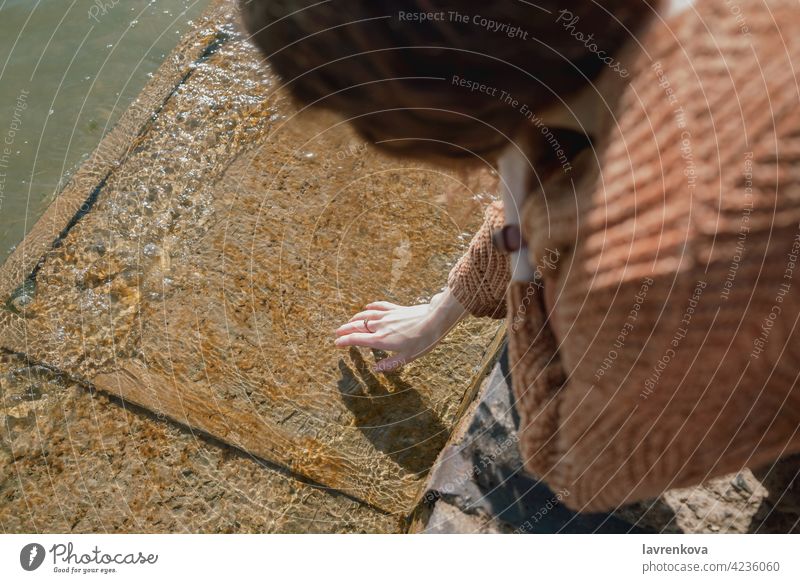 Frau berührt kaltes Wasser auf einem Steg Hand gesichtslos Strand Pier berührend Element Sauberkeit übersichtlich Pullover Rippeln Natur im Freien friedlich See