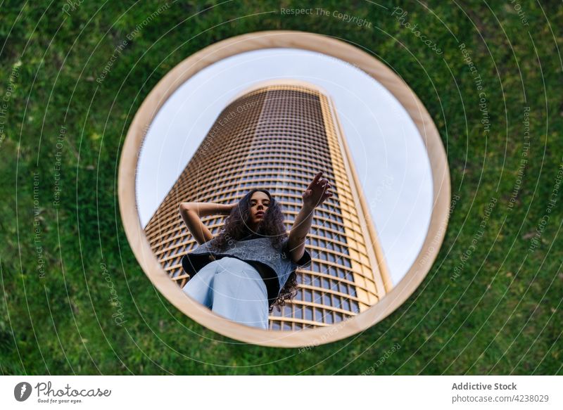 Attraktive Frau steht in der Nähe eines modernen Wolkenkratzers und spiegelt sich im Spiegel Reflexion & Spiegelung kreativ Turm Architektur Stil urban