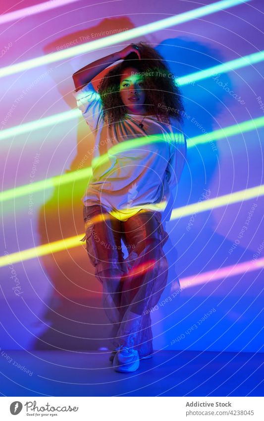 Trendige ethnische Tänzerin im Neonlicht stehend Frau Stil selbstbewusst cool neonfarbig Sonnenbrille Energie Körperhaltung informell fettarm jung Wand