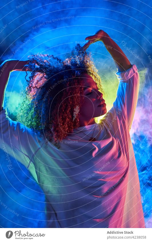 Wunderschöne schwarze Frau berührt lockiges Haar in Neonlicht Haare berühren Tanzen Energie neonfarbig cool Augen geschlossen krause Haare Bewegung ausführen