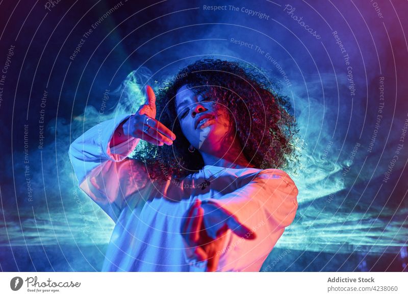 Attraktive schwarze Frau streckt die Arme zur Kamera im Tanzstudio aus Stil Tanzen ausdehnen cool Tänzer neonfarbig Augen geschlossen ausführen gestikulieren