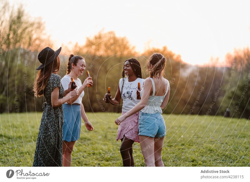Unverkennbar lächelnde multiethnische Freundinnen mit Bier im Park sprechen Freundschaft Zeit verbringen Wochenende sich[Akk] sammeln Lächeln Rasen Frauen Abend