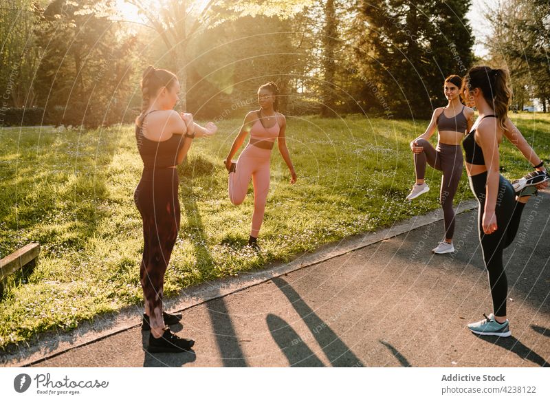 Multiethnische Sportlerinnen wärmen sich auf dem Gehweg im Stadtpark auf Aufwärmen Dehnung Training Bein angehoben Übung Park Großstadt Frauen