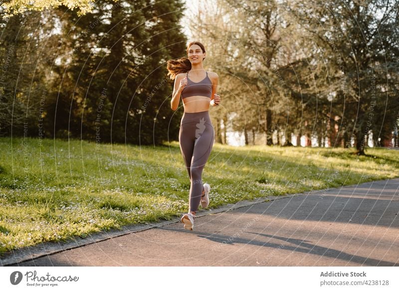 Lächelnder Läufer beim Joggen auf dem Gehweg im Park joggen Sport Herz Training Aktivität Frau Straße Asphalt Sportlerin Übung üben heiter Inhalt schnell Jogger