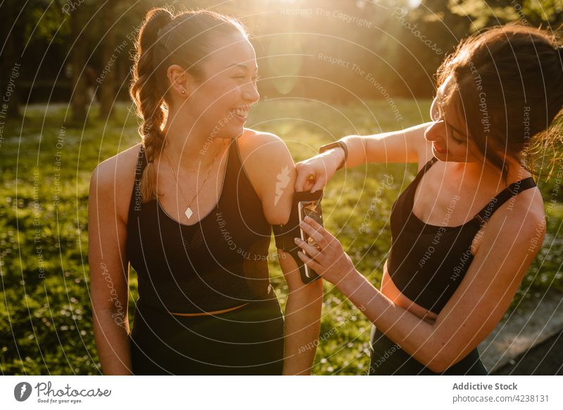 Lächelnde Sportlerin berührt Smartphone-Armband am Arm ihrer Freundin Sportlerinnen angezogen Armbinde Hilfsbereitschaft heiter reden Freundschaft Sonnenschein