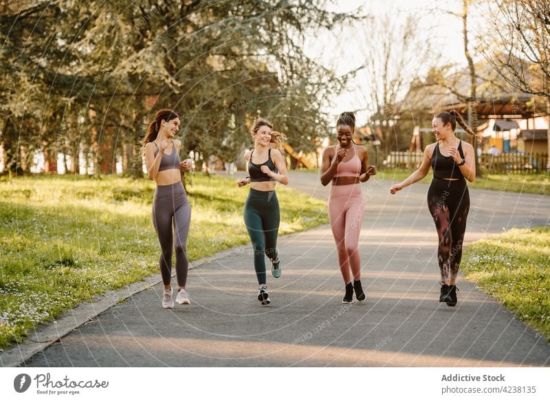 Fröhliche, bunt gemischte Sportlerinnen laufen auf einem Fußweg in einem Stadtpark Läufer joggen Training Herz Aktivität reden Frauen Park heiter Aufwärmen