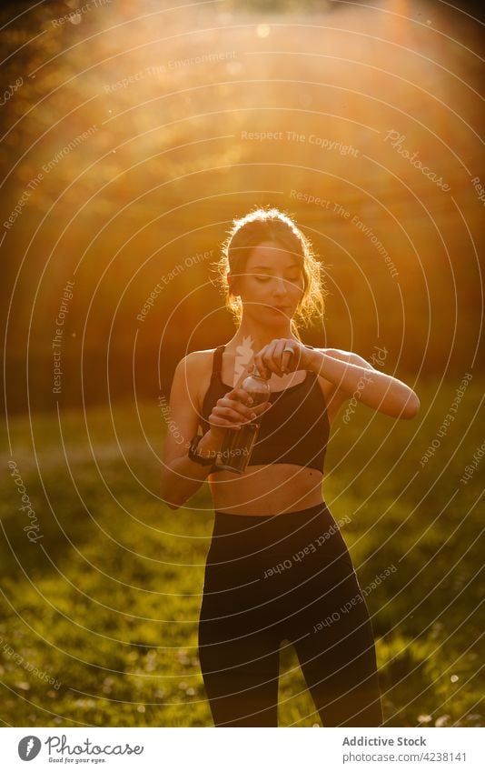 Sportler trinkt Wasser bei Sonnenschein Athlet Flasche trinken intelligente Uhr Herzschlag prüfen Pause Frau benutzend Gerät Wiese Sportlerin bewerten Training