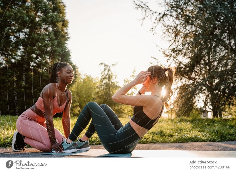 Multiracial fit Frauen tun Übungen im Park Sportlerinnen Training Zusammensein Athlet Unterleib Bauchmuskeln knirschen Hilfsbereitschaft schwarz Afroamerikaner