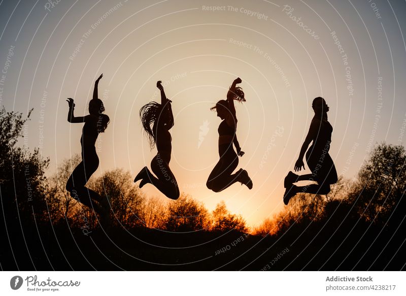 Gesellschaft unkenntlicher Frauen, die bei Sonnenuntergang im Park springen Silhouette Menschengruppe sorgenfrei Freiheit Moment aktiv Zusammensein Abend Freund