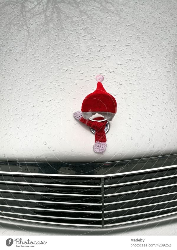 Kostüm eines Weihnachtsmanns mit Zipfelmütze auf der Kühlerfigur einer berühmten deutschen Automarke mit Kühlergrill und Regentropfen auf der Motorhaube in Lemgo bei Detmold in Ostwestfalen-Lippe