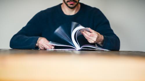 Mann blättert in einem Buch blättern Nachschlagen lesen Bildung lernen Tisch sitzen anonym Buchseiten Wissen