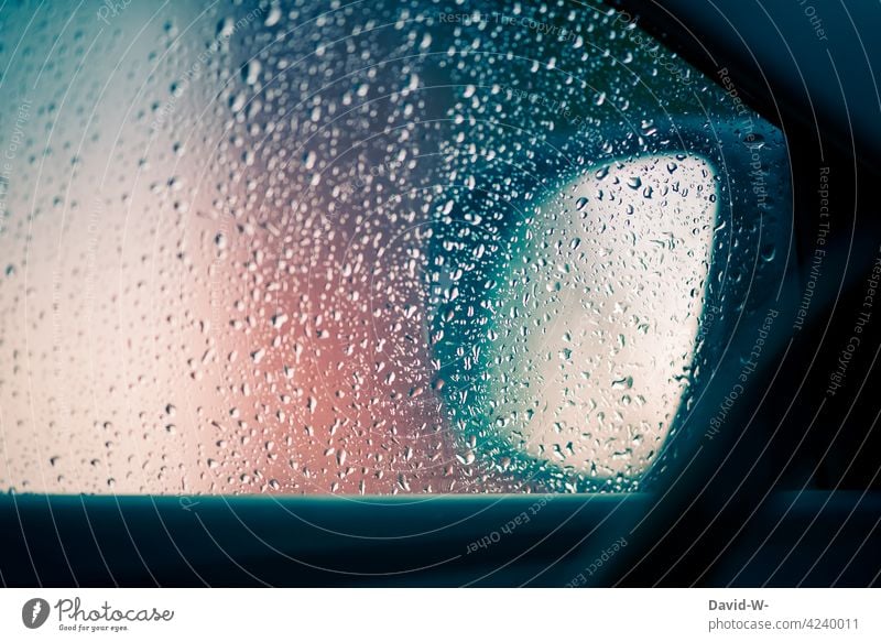 Regentropfen auf einer Scheibe eines Autos Regenwetter schlechtes Wetter Autoscheibe Unwetter Straßenverkehr Herbst nass Wassertropfen PKW Autospiegel