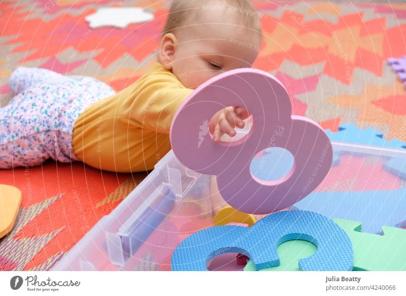 Krabbelndes Baby spielt mit Schaumstoffzahlen auf einem bunten Teppich im Freien; es hält die Zahl 8 Schaumstofffliesen zählen Nummer Unterlage Geduldsspiel