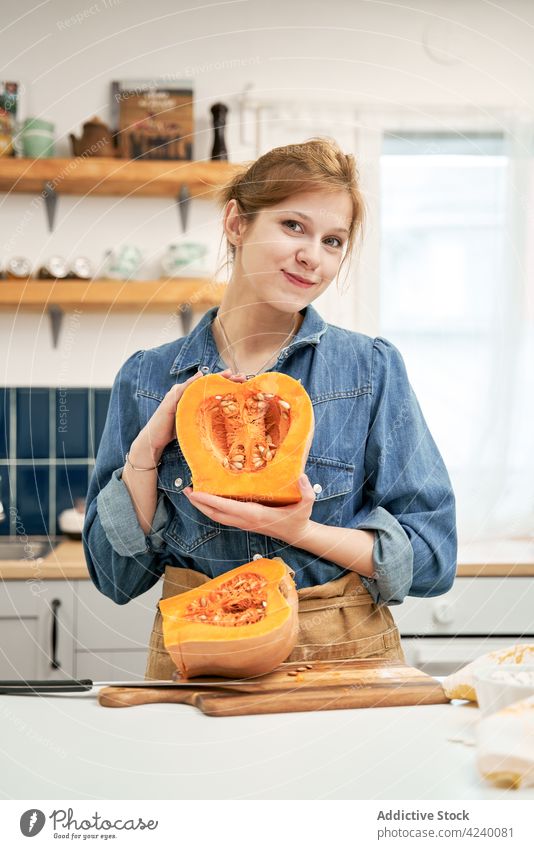 Lächelnde Frau zeigt geschnittenen Kürbis am Küchentisch Gemüse Veganer Koch Vitamin Porträt zeigen zufrieden Inhalt heiter Hälfte Samen Zellstoff Squash roh