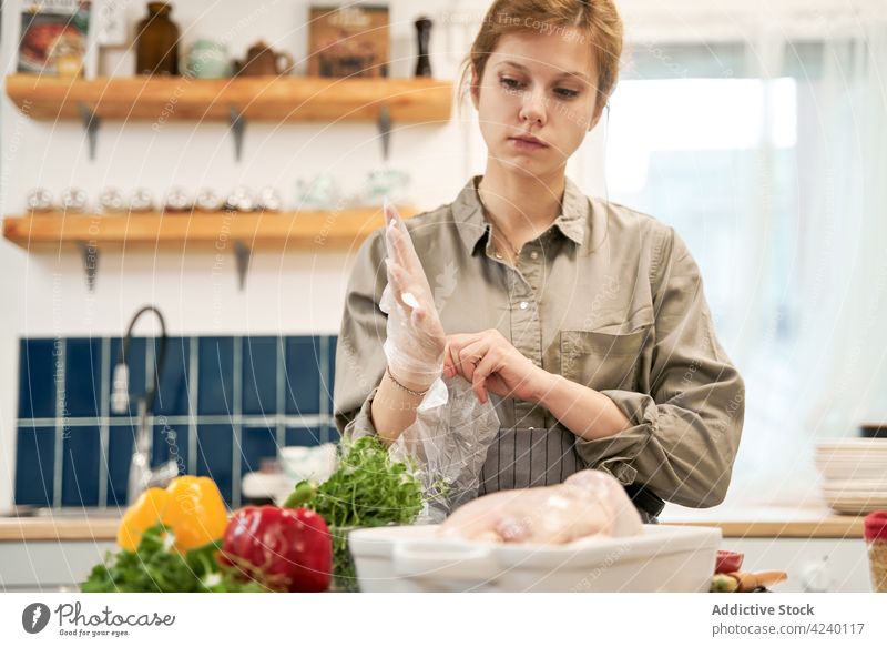Crop-Frau zieht beim Kochen in der Küche Einweghandschuhe an angezogen Handschuh Paprika Hähnchen kulinarisch Rezept Porträt Einwegartikel durchsichtig Gemüse