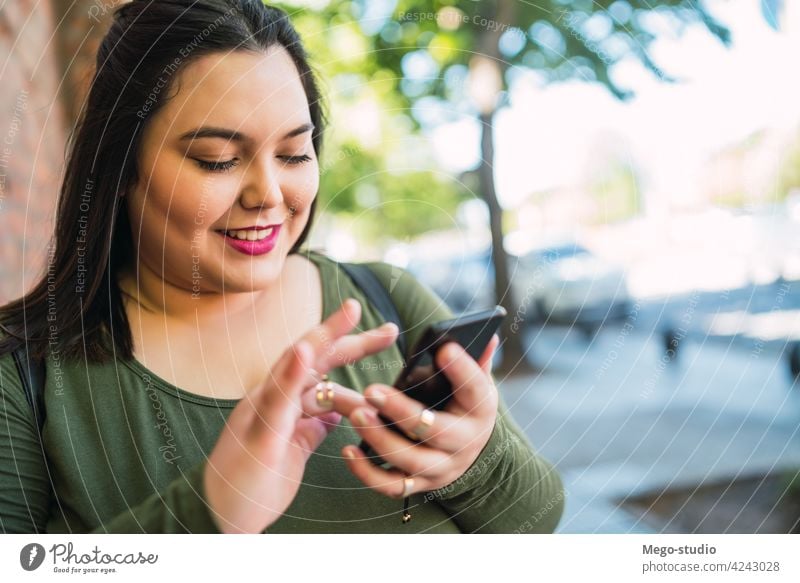 Junge Frau mit Übergröße, die ihr Mobiltelefon benutzt. Plus-Size Straße Smartphone Telefon Großstadt Mobile Menschen urban klug Funktelefon Text jung SMS