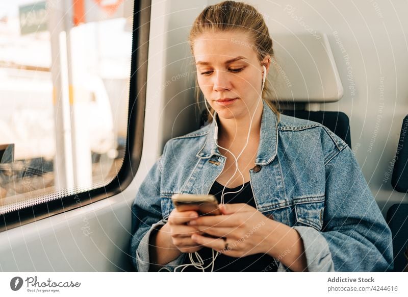Frau hört Musik und surft auf dem Handy im Zug Mitfahrgelegenheit Arbeitsweg zuhören Kopfhörer Smartphone Passagier Verkehr soziale Netzwerke benutzend Telefon
