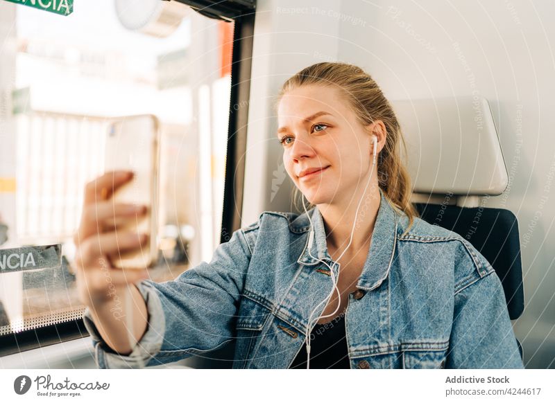 Lächelnde Frau macht Selfie im Zug unter Mitfahrgelegenheit Arbeitsweg Musik zuhören Kopfhörer Smartphone Passagier Verkehr soziale Netzwerke benutzend Telefon