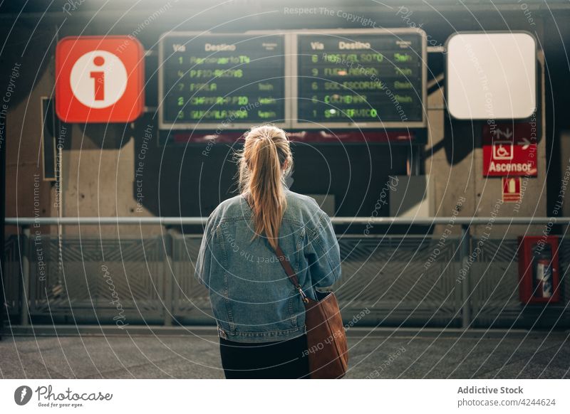 Frau auf einem Bahnhof mit Zugfahrplan Station Abheben Zeitplan Holzplatte Öffentlich urban Passagier warten reisen Eisenbahn elektronisch ankommen Information