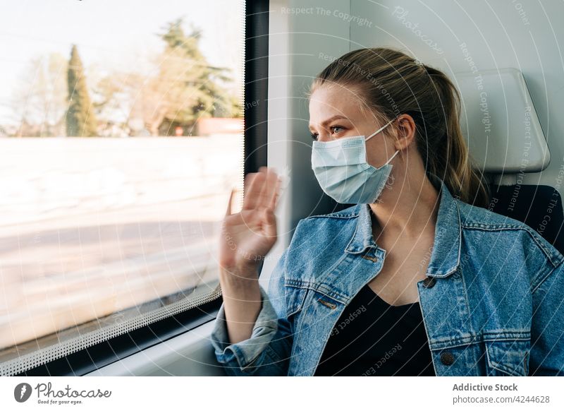 Frau mit Maske winkt vom Zug aus mit der Hand im Fenster Mitfahrgelegenheit Passagier Wellenhand Gruß Mundschutz neue Normale gestikulieren Hallo Hi heiter