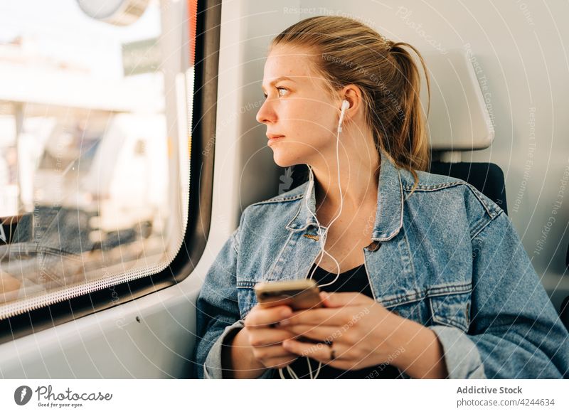 Frau hört Musik und schaut im Zug weg Mitfahrgelegenheit Arbeitsweg zuhören Kopfhörer Smartphone Passagier Verkehr soziale Netzwerke benutzend Telefon Mobile