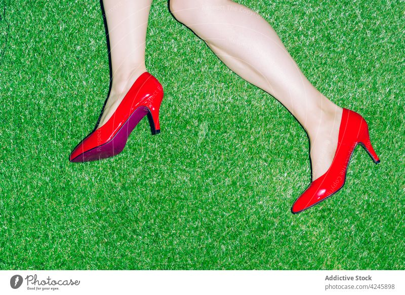 Frau in modischen roten Schuhen auf Gras liegend Mode Stil Rasen Ferse elegant Stoff Wiese anhaben Bekleidung Kleidungsstück farbenfroh Outfit feminin Paar Dame