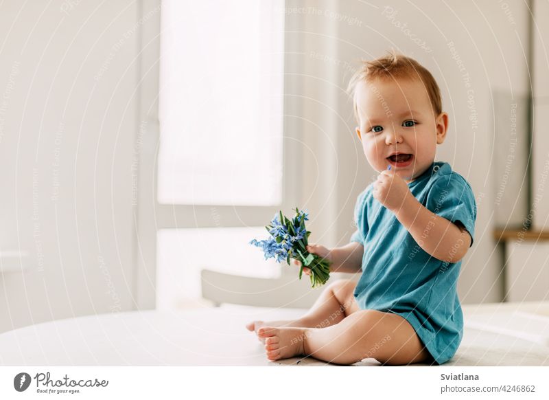 Frühlingsporträt eines Jungen mit einem Blumenstrauß. Das Baby hält Schneeglöckchen in der Hand und lächelt Kind blau Porträt wenig Liebe präsentieren