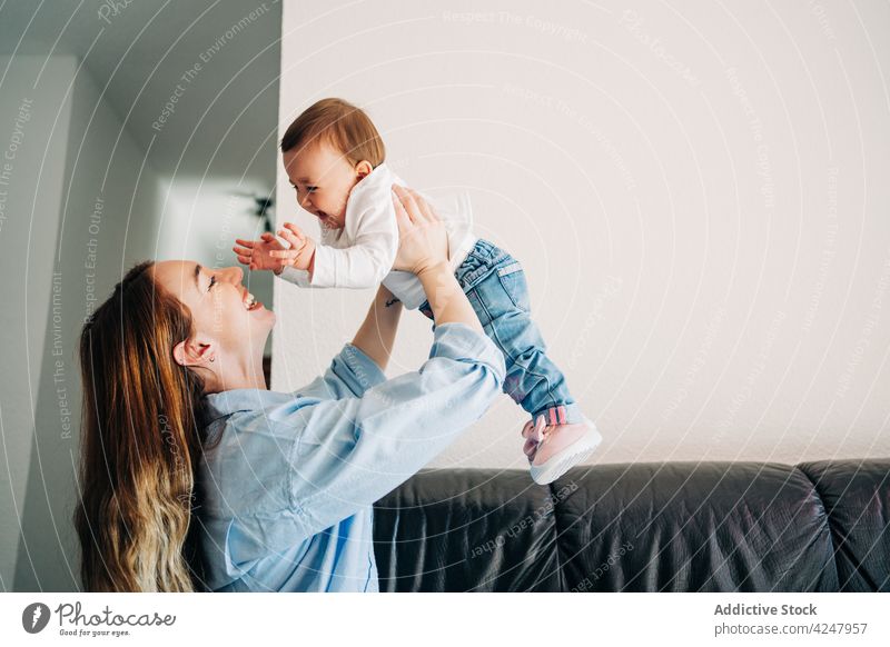 Freudige Mutter, die ihr bezauberndes Baby auf Händen trägt anheben Arme hochgezogen Lachen Zusammensein Nachkommen Pflege spielen Spaß haben Kinderbetreuung