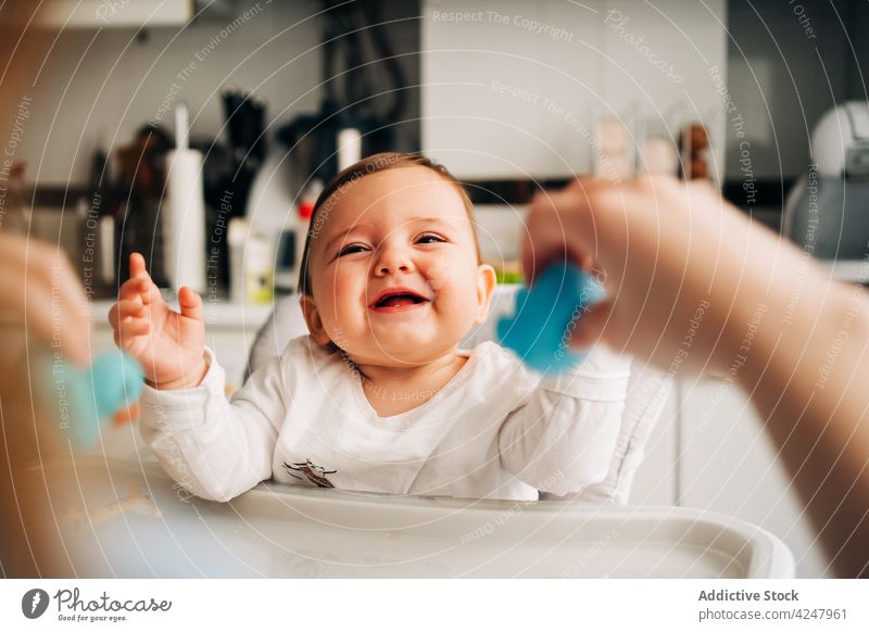 Entzückendes lächelndes Baby im Hochstuhl in der Küche sitzend füttern Lachen Lächeln Inhalt Säuglingsalter Kinderbetreuung essen Pflege heiter bezaubernd