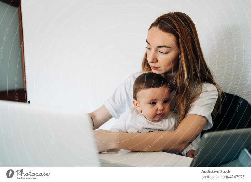 Mutter mit Laptop und Baby schaut Cartoons auf dem Tablet Zusammensein Schreibtisch Arbeit Browsen Glück Kinderbetreuung zu Hause Säuglingsalter Frau
