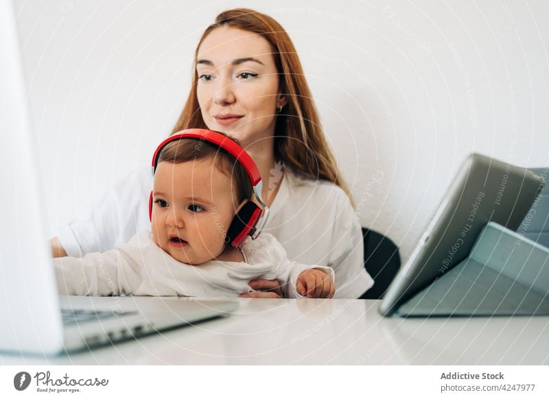 Mutter und Baby mit Kopfhörern sehen sich ein Video auf dem Laptop an zuschauen Zusammensein achtsam zuhören unterhalten Interesse neugierig Computer zu Hause