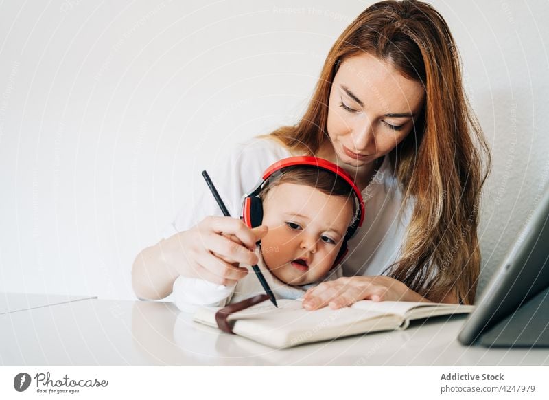 Mutter lehrt süßes Baby, in ein Heft zu schreiben zur Kenntnis nehmen lehren Schönschreibheft Entwicklung lernen Zusammensein achtsam lässig sitzen sorgsam