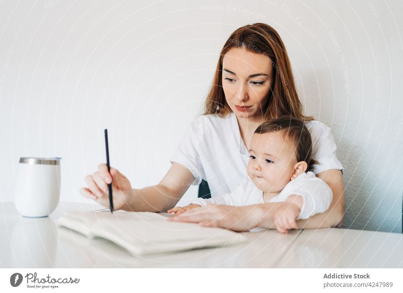 Mutter schreibt in Tagebuch und hält süßes Baby schreiben zur Kenntnis nehmen Schönschreibheft Zusammensein achtsam lässig sitzen Konzentration niedlich Frau