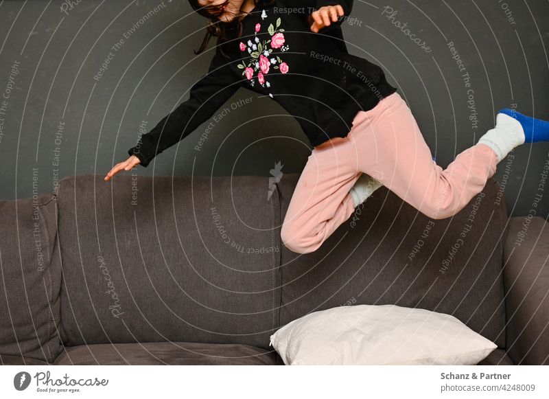 Kind springt auf die Couch spielen springen verboten ausgelassen toben blümchenpullover lebhaft frech zuhause Kindheit Spaß Kissen Mädchen Blumenmuster