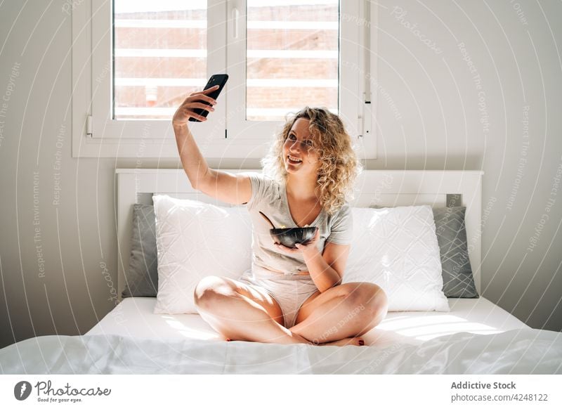 Zufriedene Frau, die ihre Mahlzeit fotografiert und auf dem Bett sitzt fotografieren Smartphone Selfie Selbstportrait Frühstück Inhalt Morgen froh lecker essen