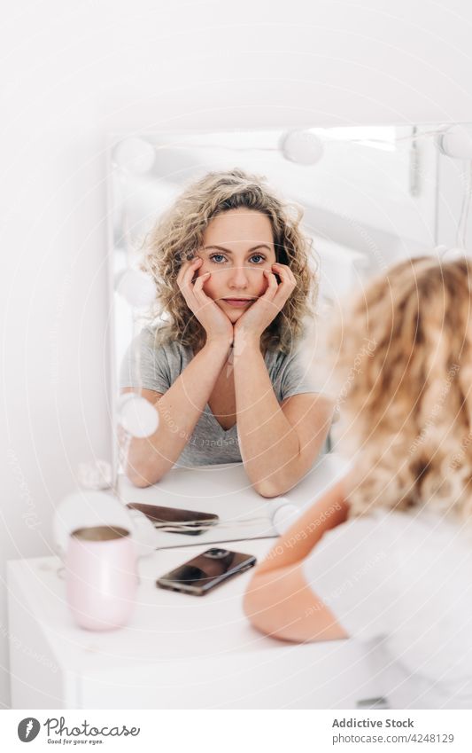 Ruhige Frau, die ihr Gesicht berührt und in den Spiegel schaut achtsam Reflexion & Spiegelung Gesicht berühren Waschtisch Schlafzimmer Windstille nachdenklich