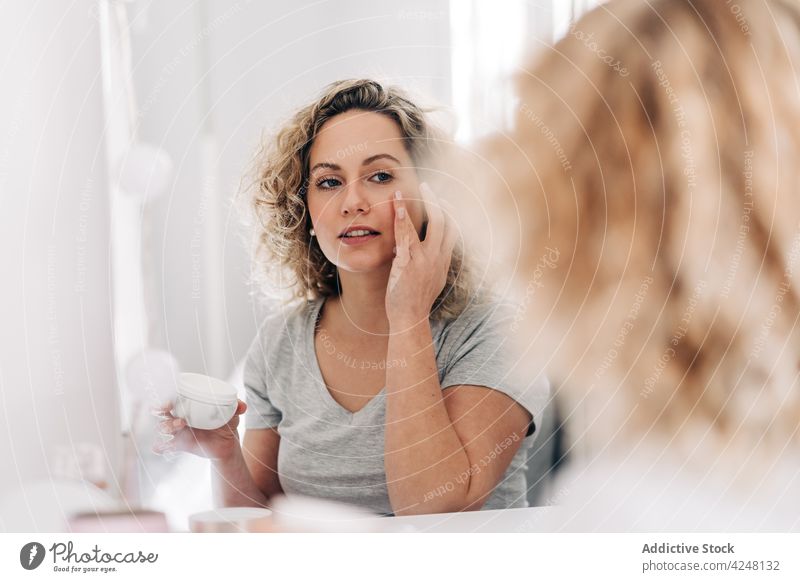 Positive Frau, die Verjüngungscreme auf das Gesicht aufträgt Sahne Gesichtsbehandlung bewerben Hautpflege Reflexion & Spiegelung verwöhnen Waschtisch verjüngen
