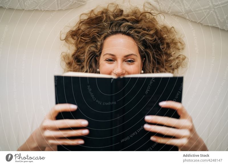 Frau, die auf dem Bett liegend ein Buch liest lesen Lügen ruhen heimwärts Glück Komfort Leseratte LAZY Wochenende sich[Akk] entspannen Freude jung krause Haare