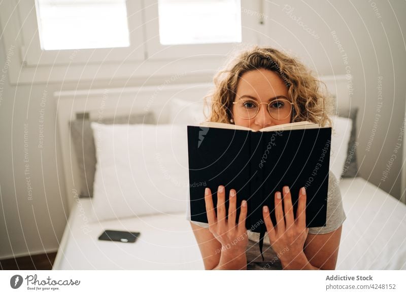 Glückliche junge Frau liest einen Roman und ruht sich auf dem Bett aus lesen Buch Lächeln Freizeit Hobby Leseratte interessant sich[Akk] entspannen krause Haare