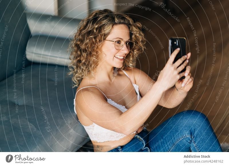Positive junge Frau sitzt auf dem Boden und macht ein Selfie mit ihrem Smartphone Lächeln positiv selbstsicher Stil soziale Netzwerke heimwärts selbstbewusst