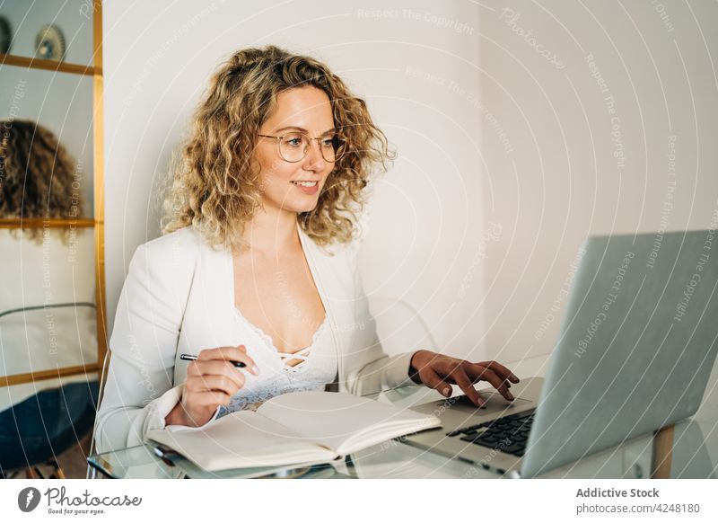 Junge Frau schreibt in ein Notizbuch und arbeitet zu Hause am Laptop zur Kenntnis nehmen Arbeit freiberuflich Glück schreiben Lächeln abgelegen online Internet