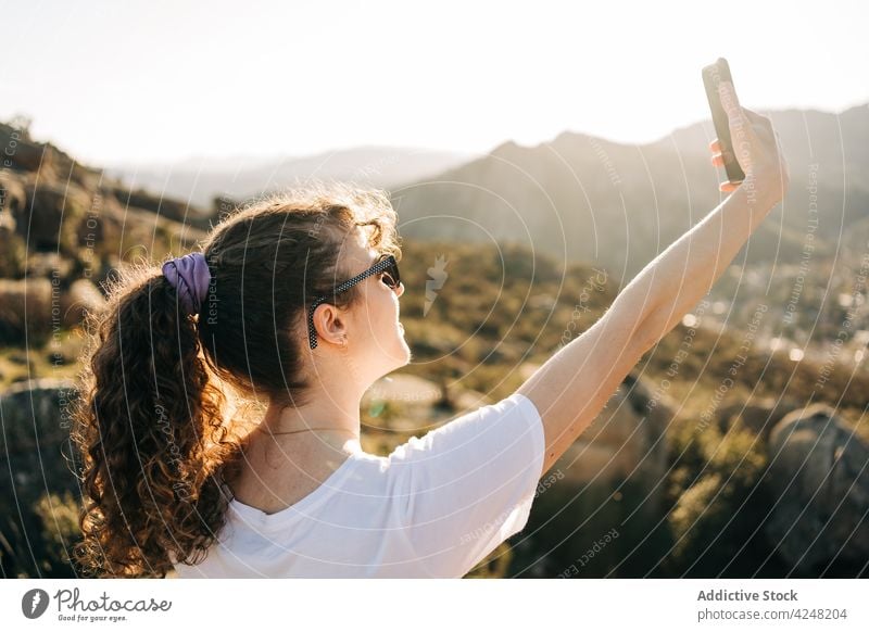 Zufriedene junge Frau macht ein Selfie im Urlaub in den Bergen Reisender fotografieren Glück Berge u. Gebirge Tourismus Smartphone reisen lässig Sonnenbrille