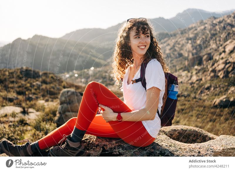 Lächelnde junge Frau sitzt auf einem Stein und bewundert die Natur in einem Gebirgstal bewundern Berge u. Gebirge sich[Akk] entspannen genießen Reisender Urlaub