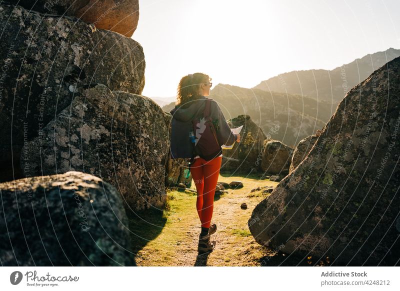 Anonyme Frau beim Kartenlesen inmitten von Felsformationen während einer Wanderung Landkarte Felsbrocken Reisender Spaziergang Trekking Lächeln sich orientieren