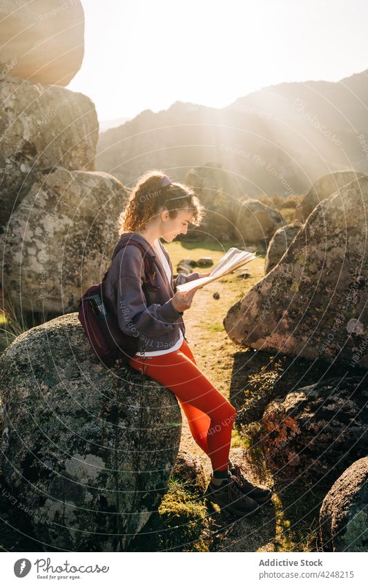 Fröhliche junge Frau beim Kartenlesen inmitten von Felsformationen während einer Wanderung Landkarte Felsbrocken Reisender Trekking Lächeln sich orientieren