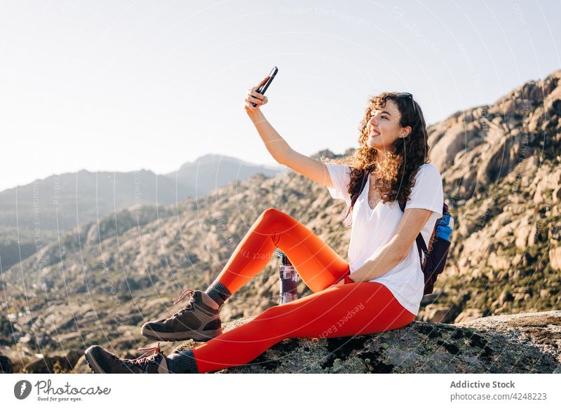 Fröhliche junge Rucksacktouristin macht ein Selfie auf einem Berghang im Sonnenlicht Frau Lächeln Reisender Smartphone erkunden Berge u. Gebirge Trekking